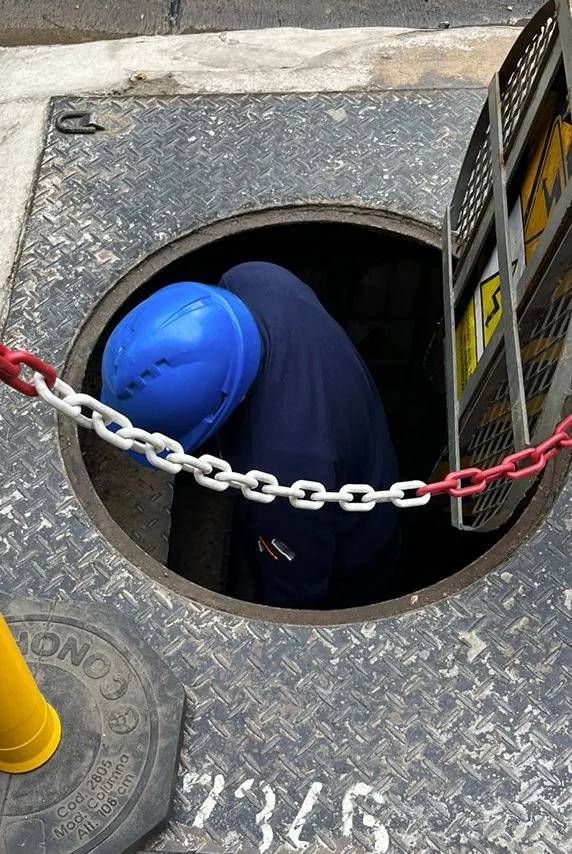 Technician in a hard hat entering an underground vault through the manhole